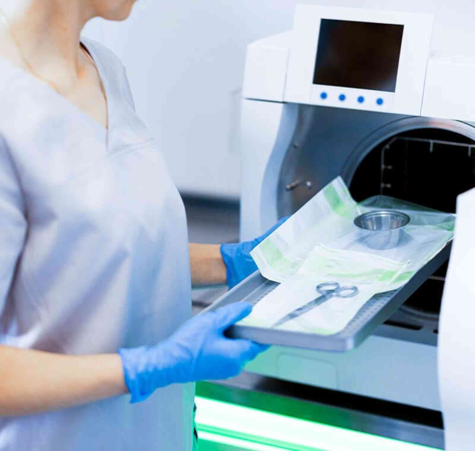 A surgical sterile processing technician wearing gloves and scrubs organizes and inspects surgical instruments laid out on a sterile drape in a hospital central-sterile department.
